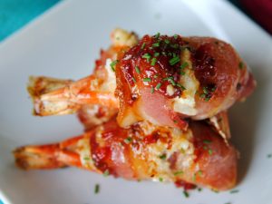 Bacon Wrapped Crab Stuffed Shrimp Garnished with Chives on a White Plate