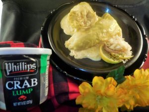 Comano Crab Cabbage Rolls on a Small Black Plate next to a tub of Phillips Lump Crab Meat