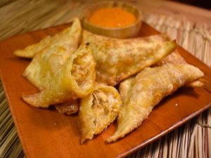 Crab and Chorizo Wonton Empanadas on a Wooden Plate with a Small Ramekin of Dipping Sauce