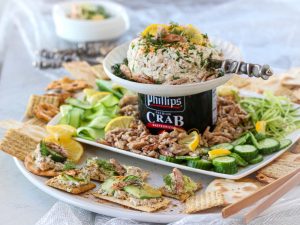 Crabby Cucumber Dill Spread in a White Bowl on a Black Can of Phillips Crab Meat Surrounded by Crackers and Cucumber Slices